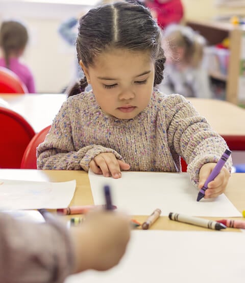 Preschool child sitting at table using crayons from Becker's Students Packs